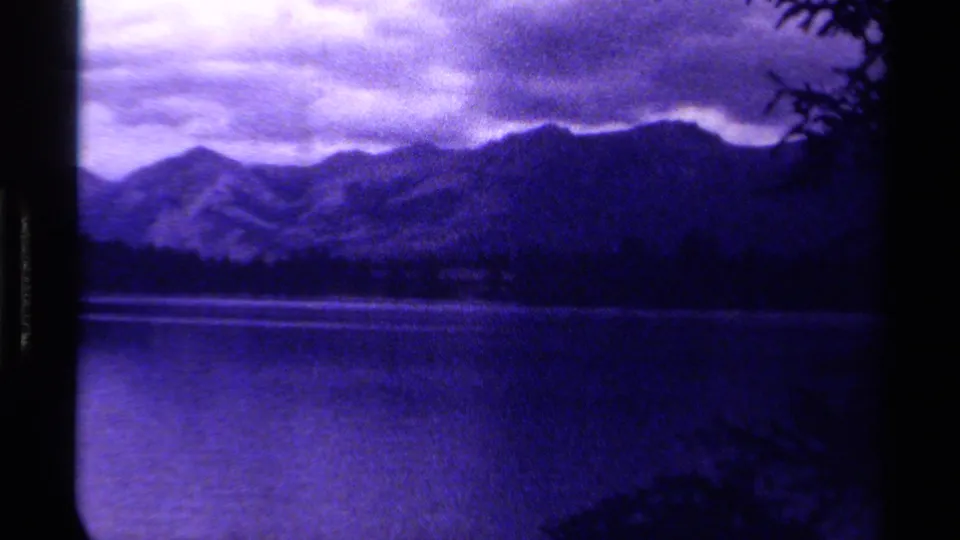 The 8mm frame shows a purple-tinted Canadian lake view with mountain ridges, low clouds, and vegetation intruding near the edge.