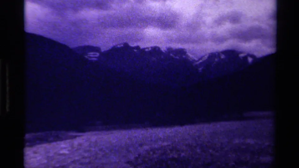 A darker 1979 Canadian mountain view shows shadowed slopes, small snow patches, cloudy sky, and a pale shoreline or water edge.