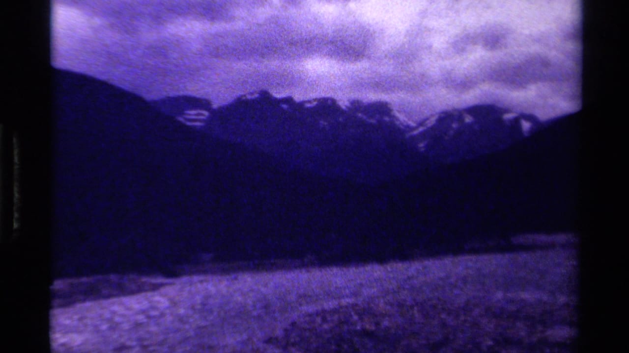 1979 Canadian 8mm frame showing a shadowed mountain range, cloudy sky, and a dim foreground river or valley edge.