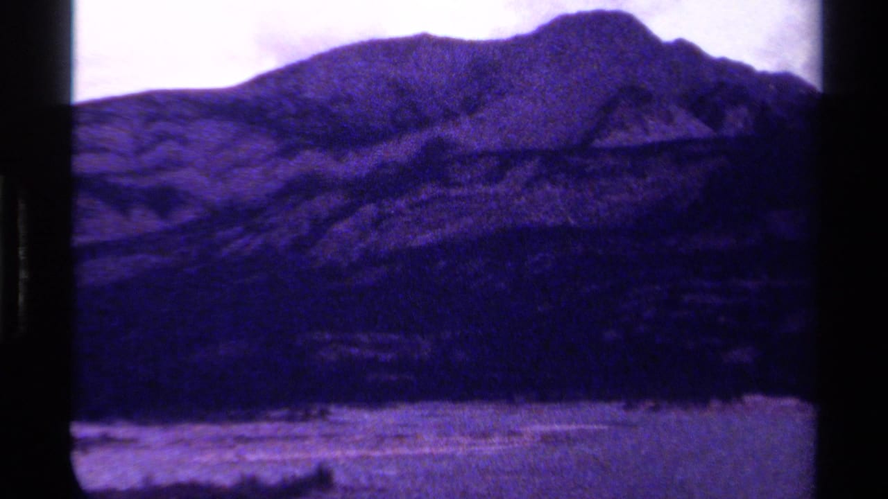 Purple-tinted mountain ridge with a pale valley below and dark film borders.
