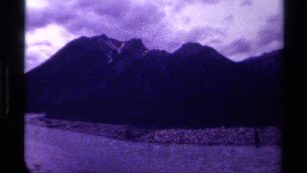 Dark mountain silhouette with water and shoreline beneath a cloudy sky.