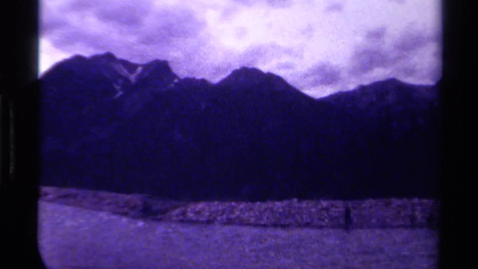 1979 Canadian 8mm frame with soft mountain peaks, a low shoreline, water, and heavy purple-blue film coloration.