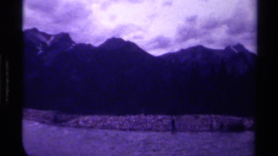 1979 Canadian 8mm frame showing a mountain ridge, cloudy sky, water, and shoreline, with pronounced grain and gate edges.
