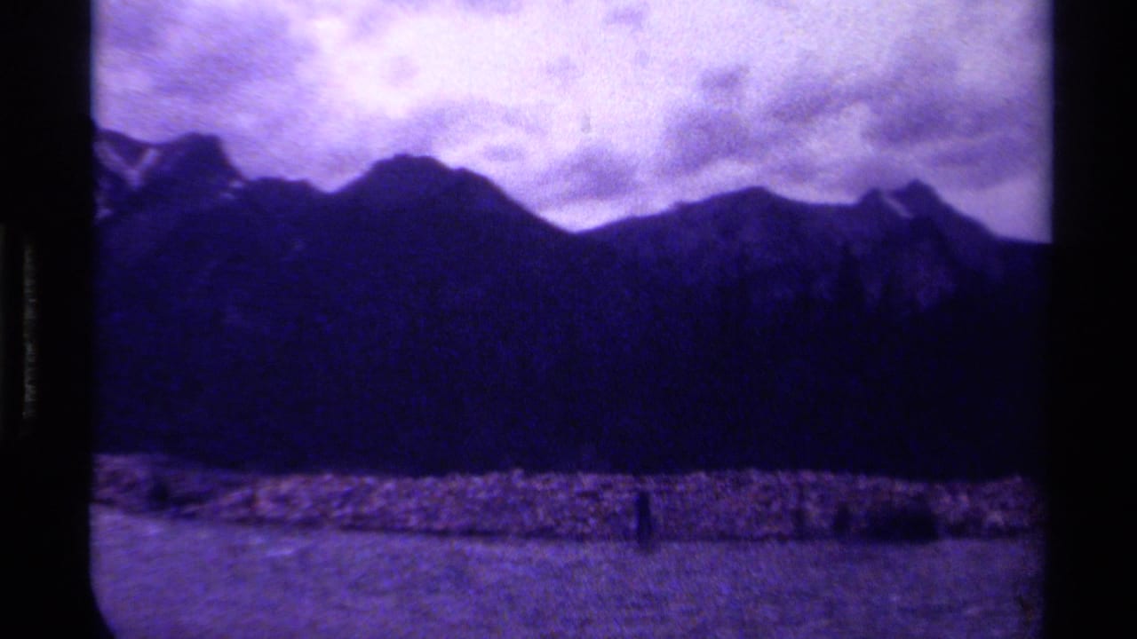 1979 Canadian 8mm frame showing silhouetted mountains, cloudy sky, and a purple-blue faded film palette.