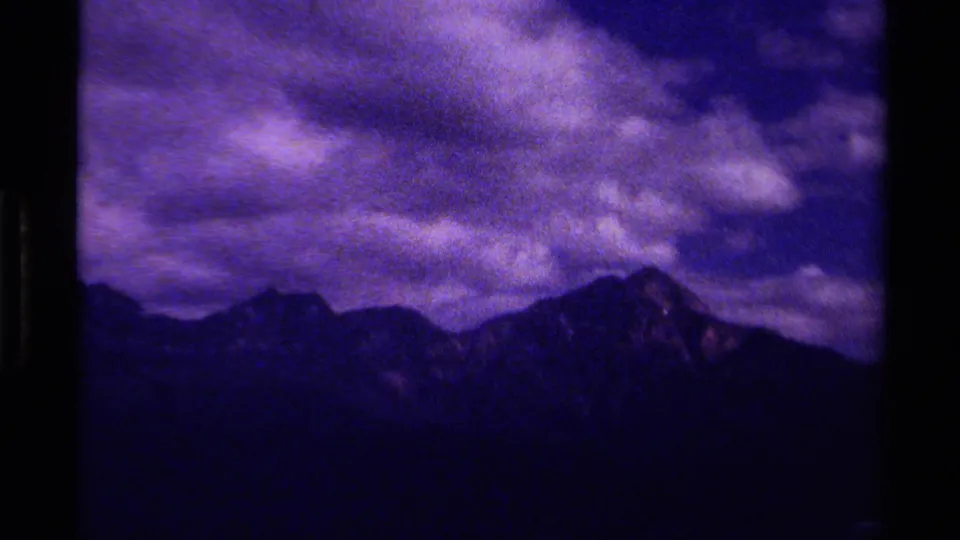 1979 Canadian 8mm frame showing shadowed peaks beneath textured storm clouds and dark film borders.