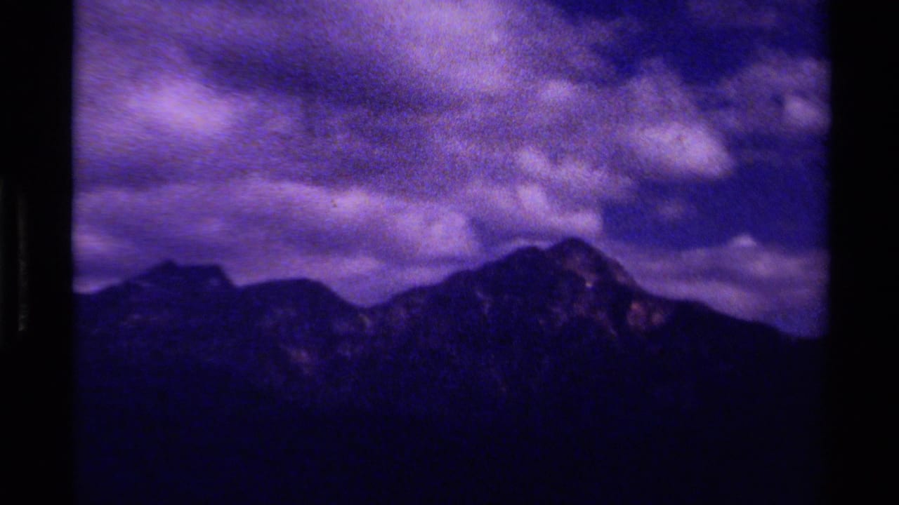 Dark mountain ridge beneath a purple-blue cloudy sky on 8mm film.