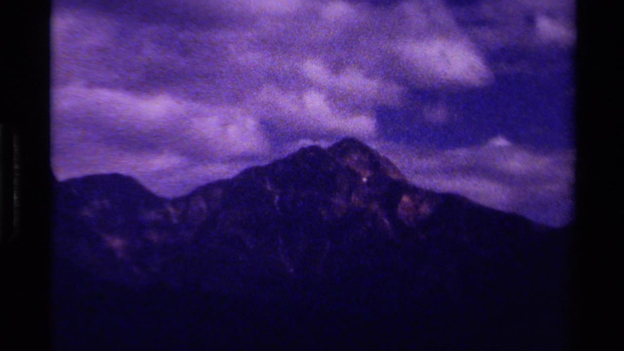 1979 Canadian 8mm frame with a dark mountain peak and layered ridges beneath a purple-toned cloudy sky.
