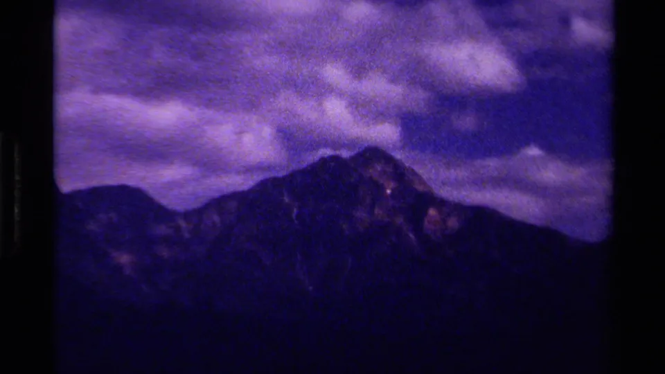 1979 Canadian 8mm frame with a dark mountain peak and layered ridges beneath a purple-toned cloudy sky.