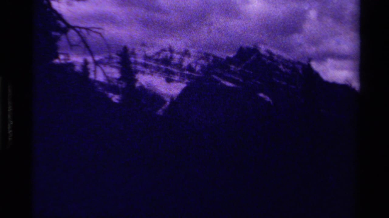 1979 Canadian 8mm frame showing shadowed mountain ridges, a cloudy purple sky, and faint evergreen silhouettes in the foreground.