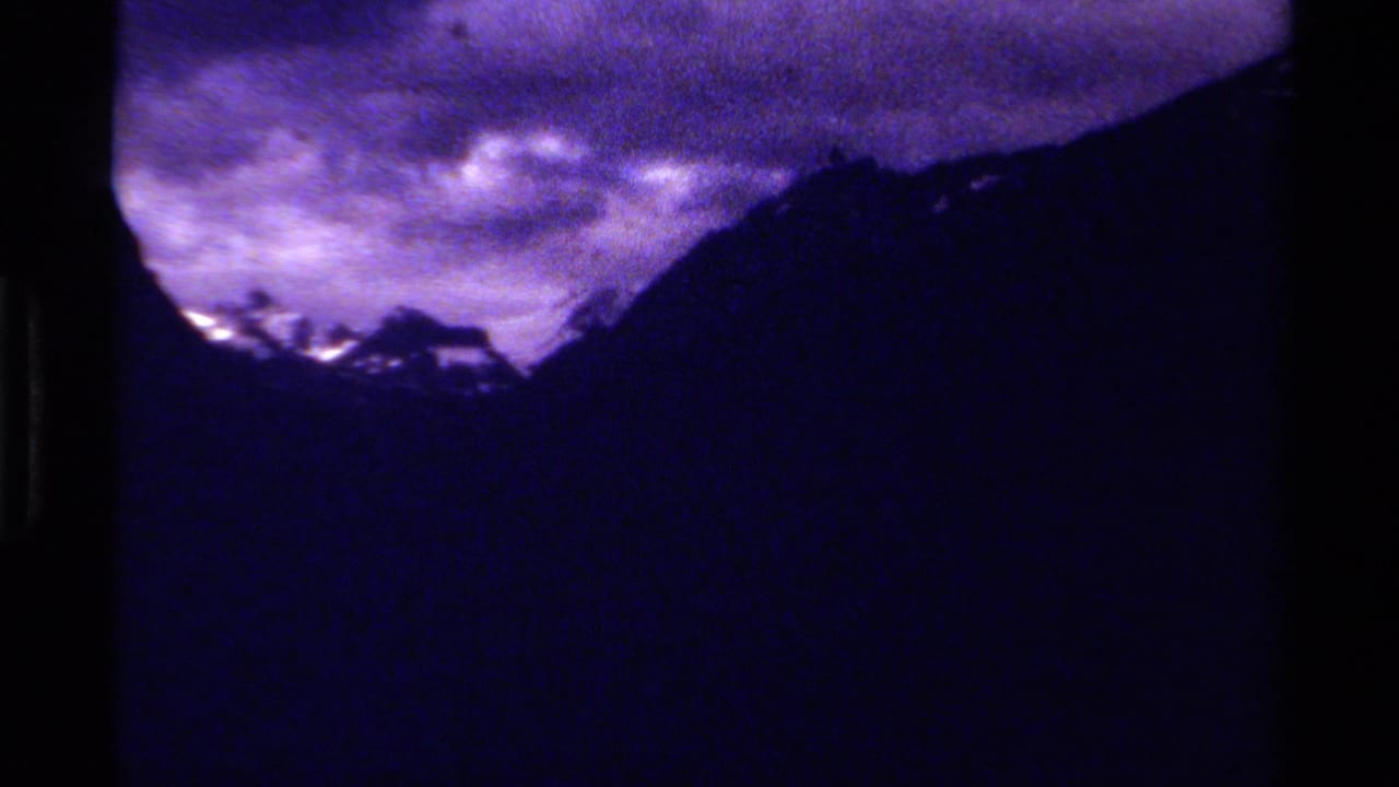 Snow-edged mountain peaks appear between dark ridges under a purple cloud bank.