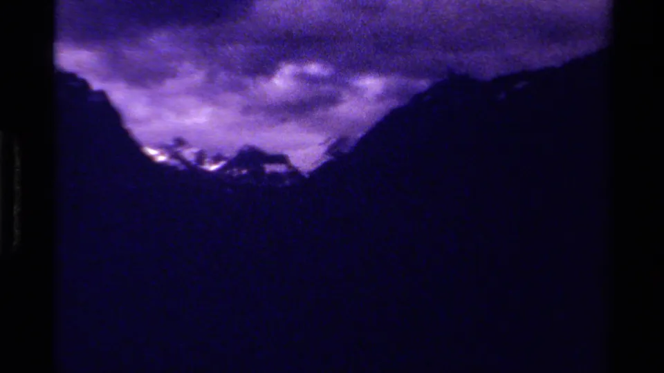 1979 Canadian 8mm frame showing a shadowed mountain valley, distant pale peaks, and heavy purple-tinted cloud cover.