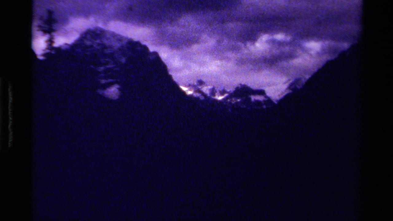 1979 Canadian mountain landscape on 8mm film, with purple color shift, cloud cover, and distant snowfields.