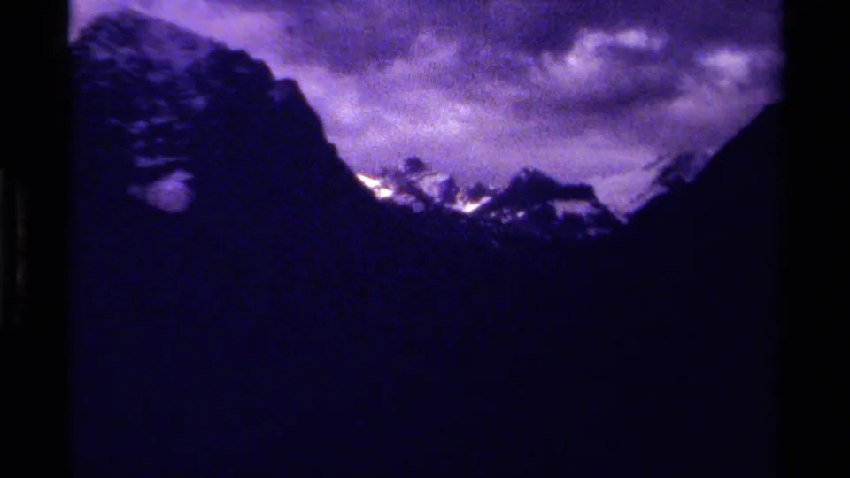 1979 Canada 8mm frame with a dark evergreen at left, mountain silhouettes, snowy peaks, and purple cloud cover.