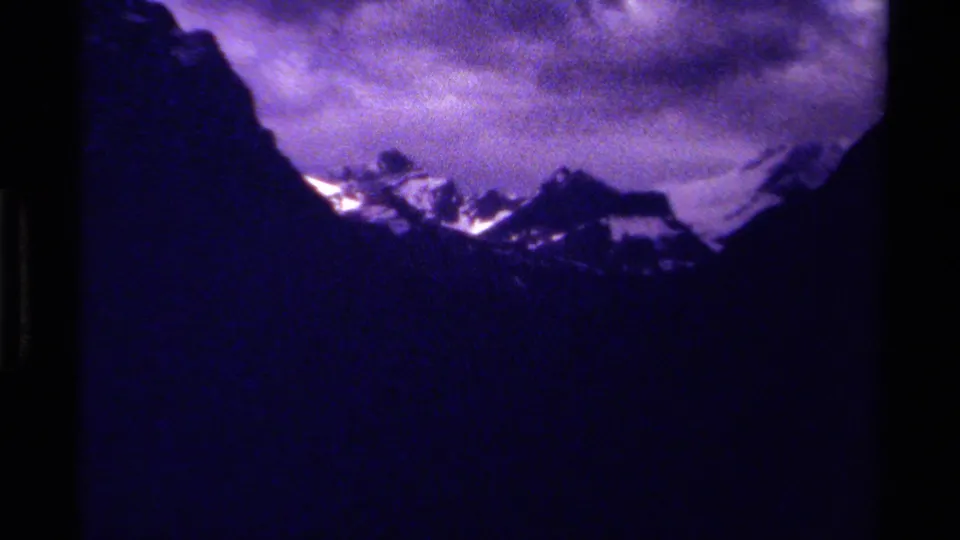 Zoomed 1979 8mm view of a Canadian snowy mountain range beneath a purple, cloudy sky.