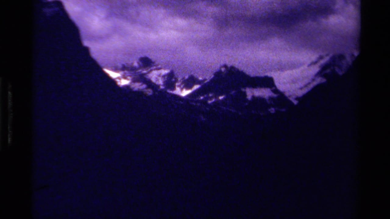 Snow-topped mountain peaks under a dark purple clouded sky.