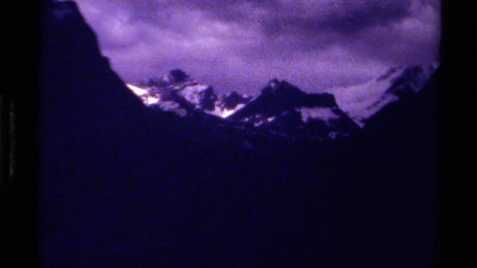 1979 8mm Canada footage showing distant snow-topped mountain peaks beneath a purple-tinged clouded sky.