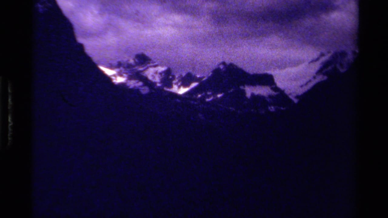 Distant snow-capped peaks framed by dark mountain slopes and clouds.