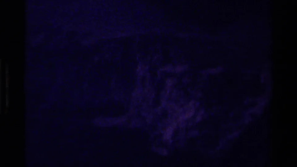 Dark, purple-shifted 8mm frame showing rugged mountain terrain with heavy shadow and visible film grain.