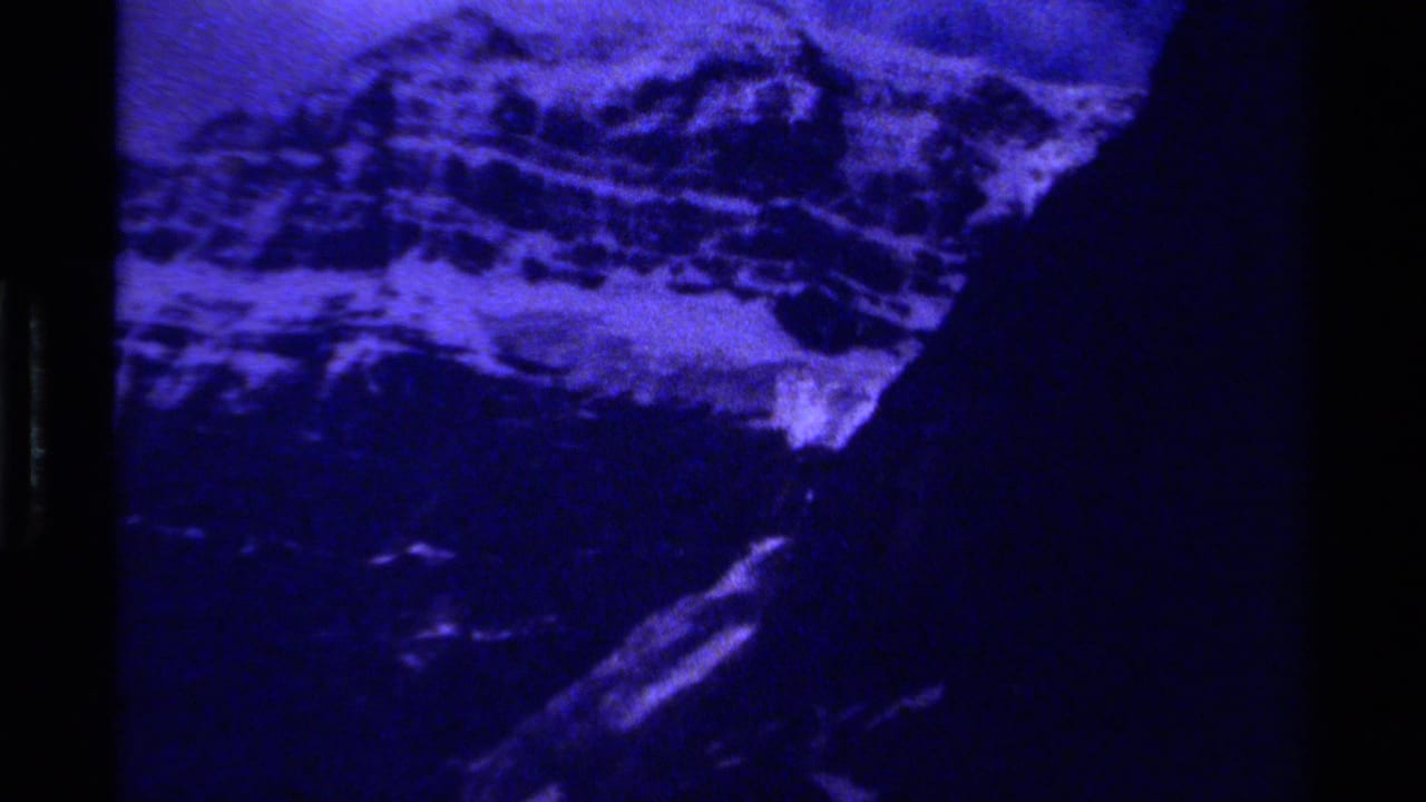 Blue monochrome mountain scene with snow, rock faces, and dark framing edges.