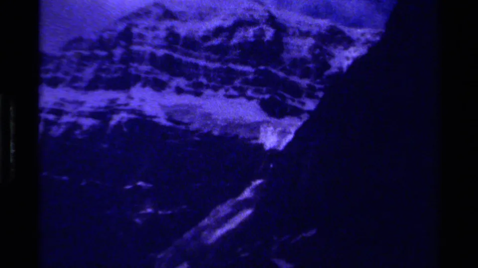 Blue-tinted 8mm view of Canadian mountain slopes, snowfields, and dark vertical film borders.