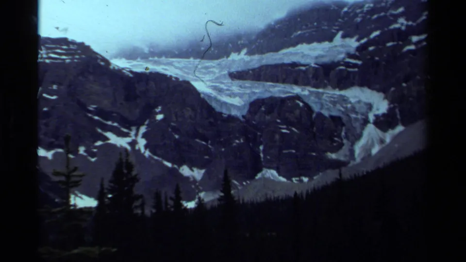 1979 Canada 8mm frame showing a pale glacier or snowfield below rocky mountains, with evergreen silhouettes in the foreground.