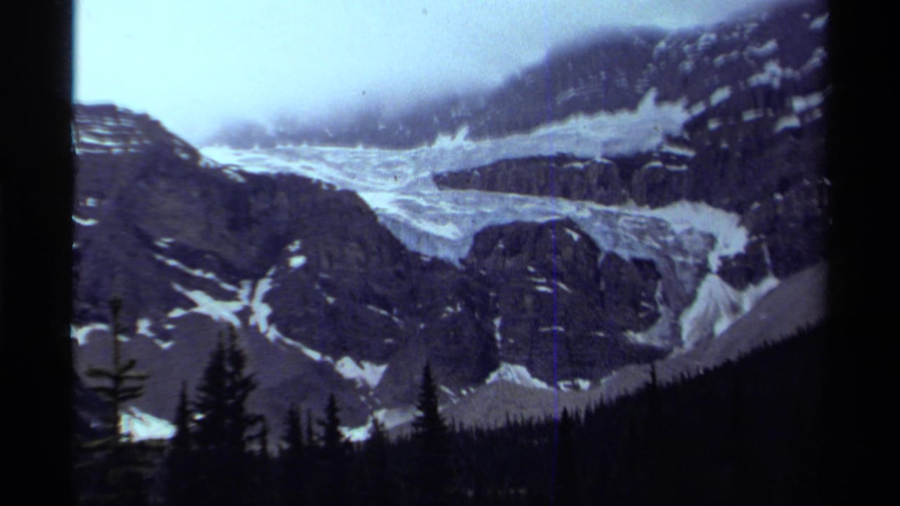 Rocky alpine slope and glacier with tree silhouettes below.