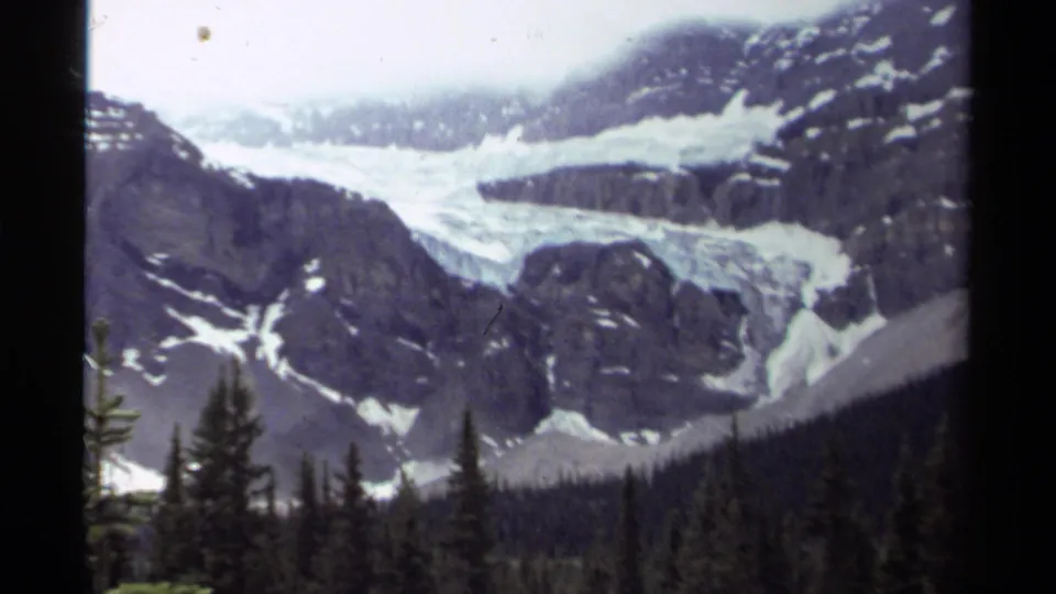 Soft 8mm frame from 1979 Canada showing a glacier between dark mountain ridges with evergreens at the bottom edge.