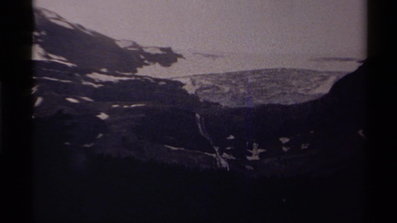 1979 8mm home-movie frame from Canada showing a dark mountain ridge, snow patches, pale sky, and a dim lake below.