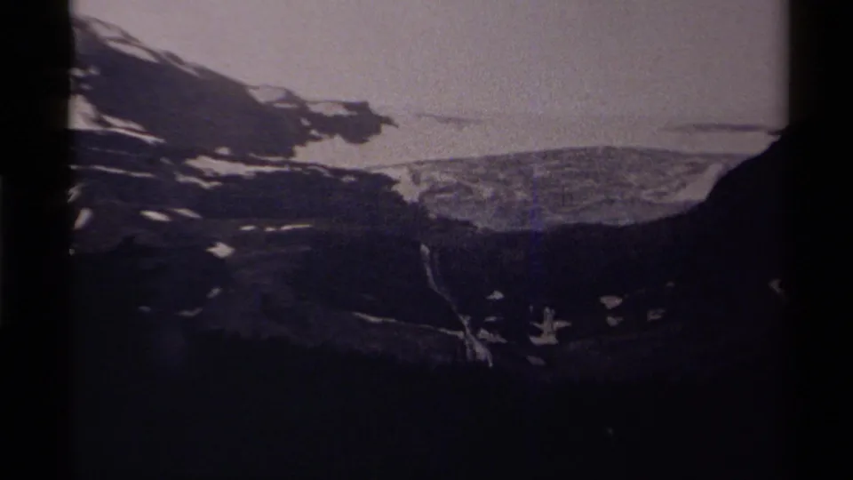 1979 8mm home-movie frame from Canada showing a dark mountain ridge, snow patches, pale sky, and a dim lake below.