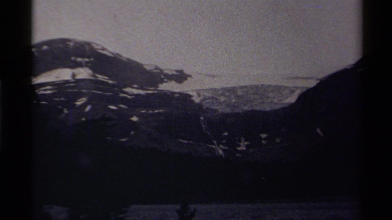 Canadian 8mm frame showing a snow-marked mountain slope, dark valley edge, and faint lake surface in low evening or night light.