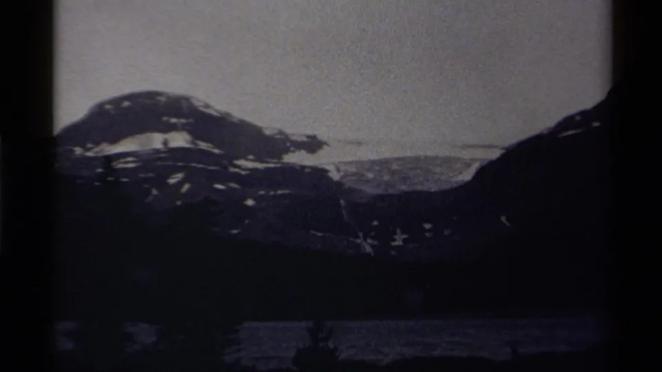 1979 Canada home-movie frame with a snow-patched mountain, dark lake, and faint foreground silhouettes in grainy low-light exposure.