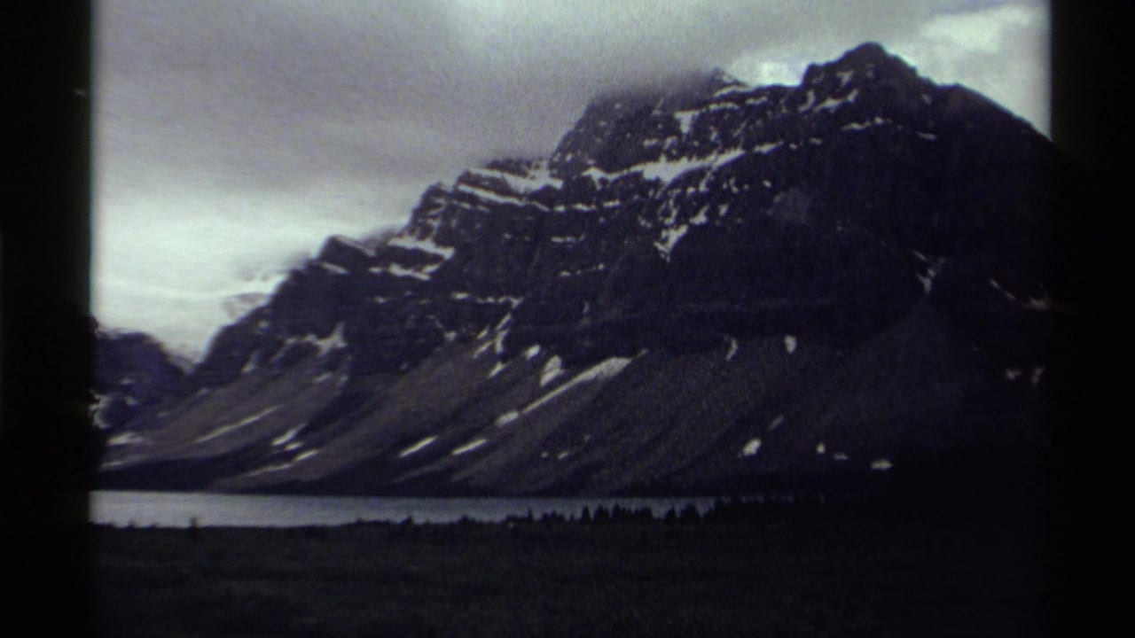 1979 8mm Canada landscape frame showing a dark snow-dusted mountain above a calm lake and forested foreground.