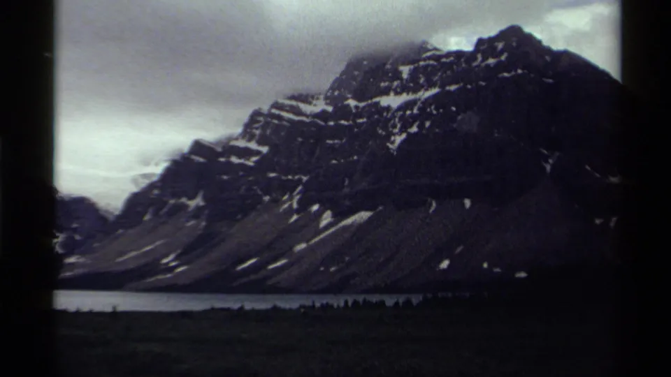 1979 8mm Canada landscape frame showing a dark snow-dusted mountain above a calm lake and forested foreground.