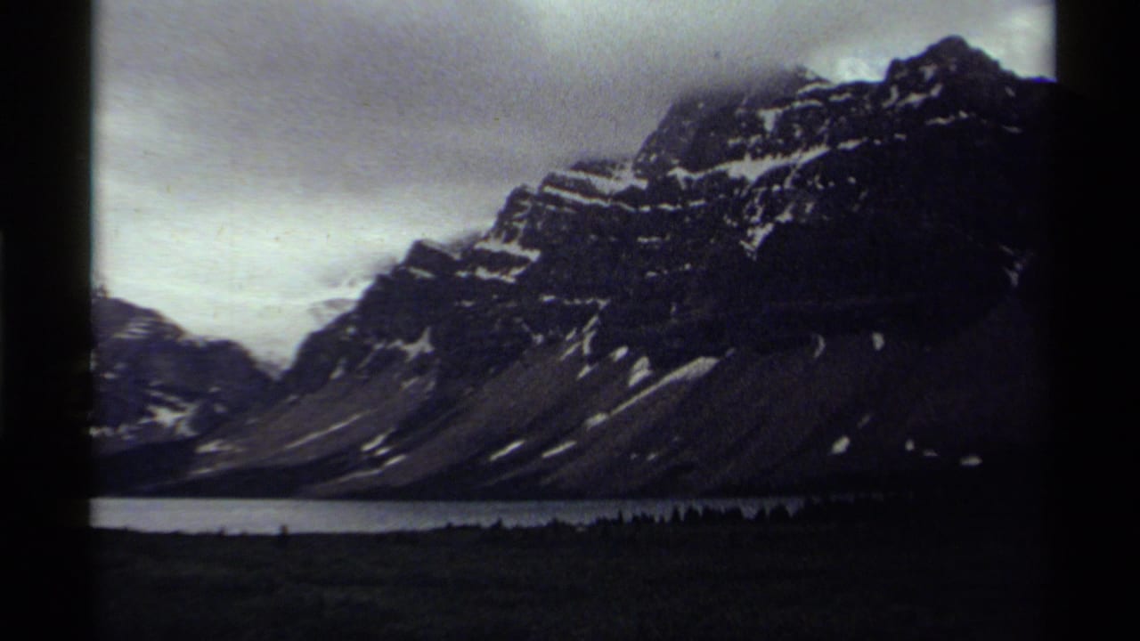 Mountain peak and lake with dark foreground beneath overcast sky.