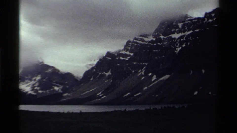 1979 Canada home-movie frame showing rugged mountain slopes, snow patches, lake water, and a dark foreground band.
