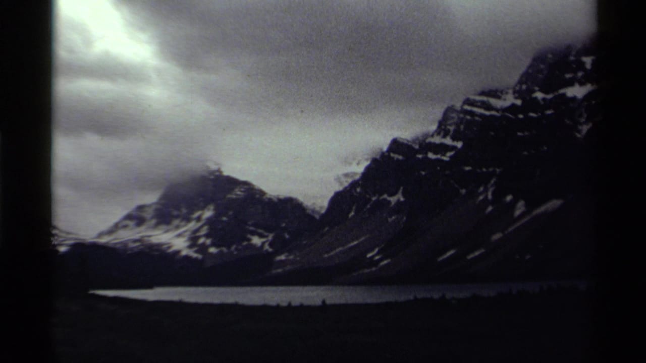 Snowy mountains above a lake beneath heavy clouds, framed by dark 8mm film borders.