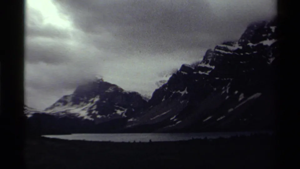 1979 8mm Canada footage showing snow-streaked mountains over a lake under dramatic cloud cover.
