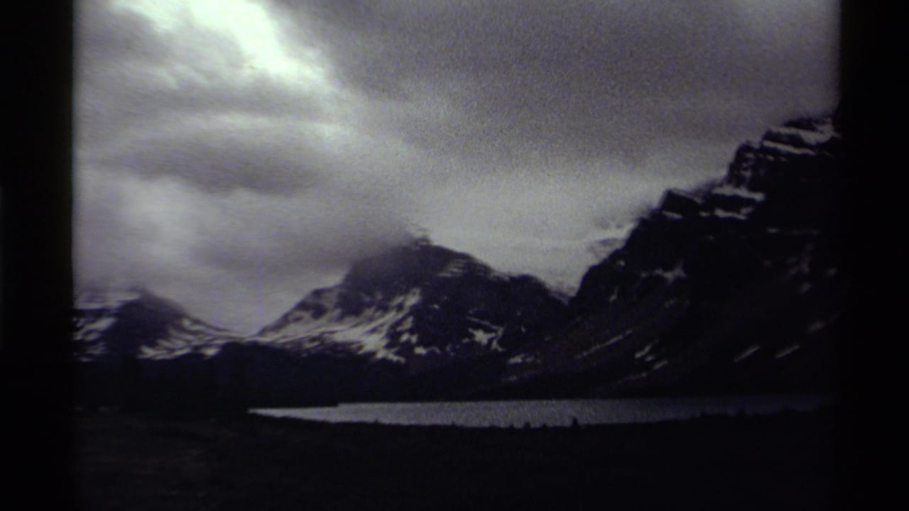 Mountain ridge and lake under overcast sky with dark film-edge borders visible.