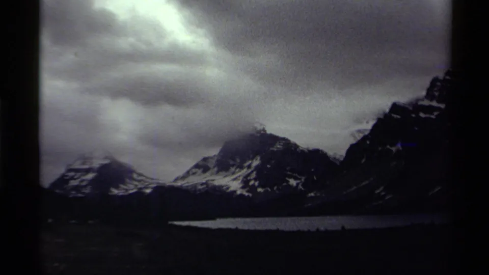 1979 Canada 8mm frame with a broad overcast sky above snowy mountains and a lake below.