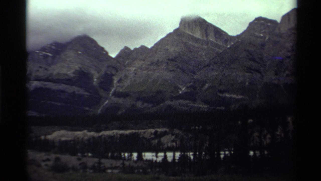 Dark mountain peaks under low cloud with forest and water below.