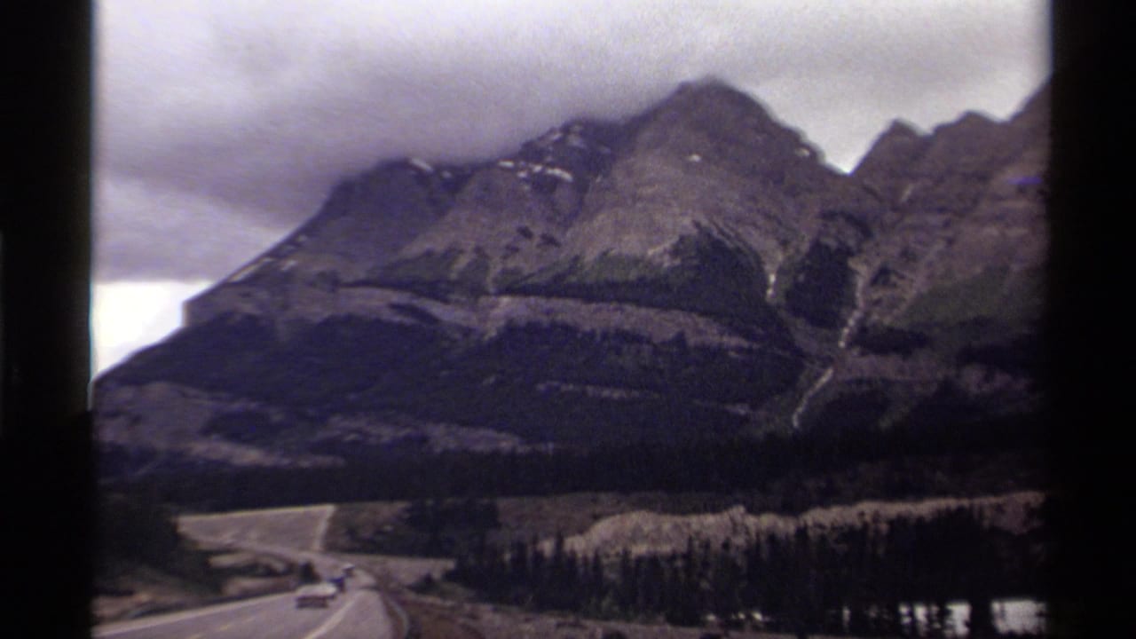 Cloudy mountain landscape with a road curving through forested terrain.