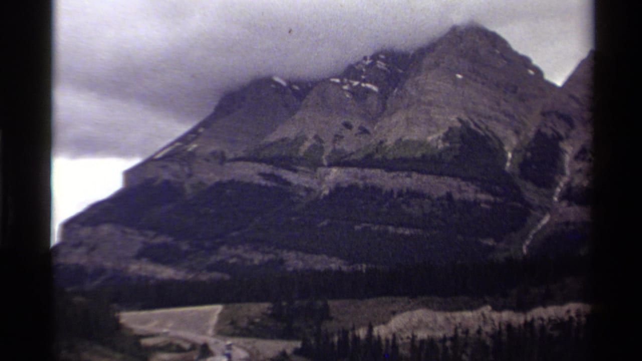 Rocky mountain peak above a road and dark evergreen hills.