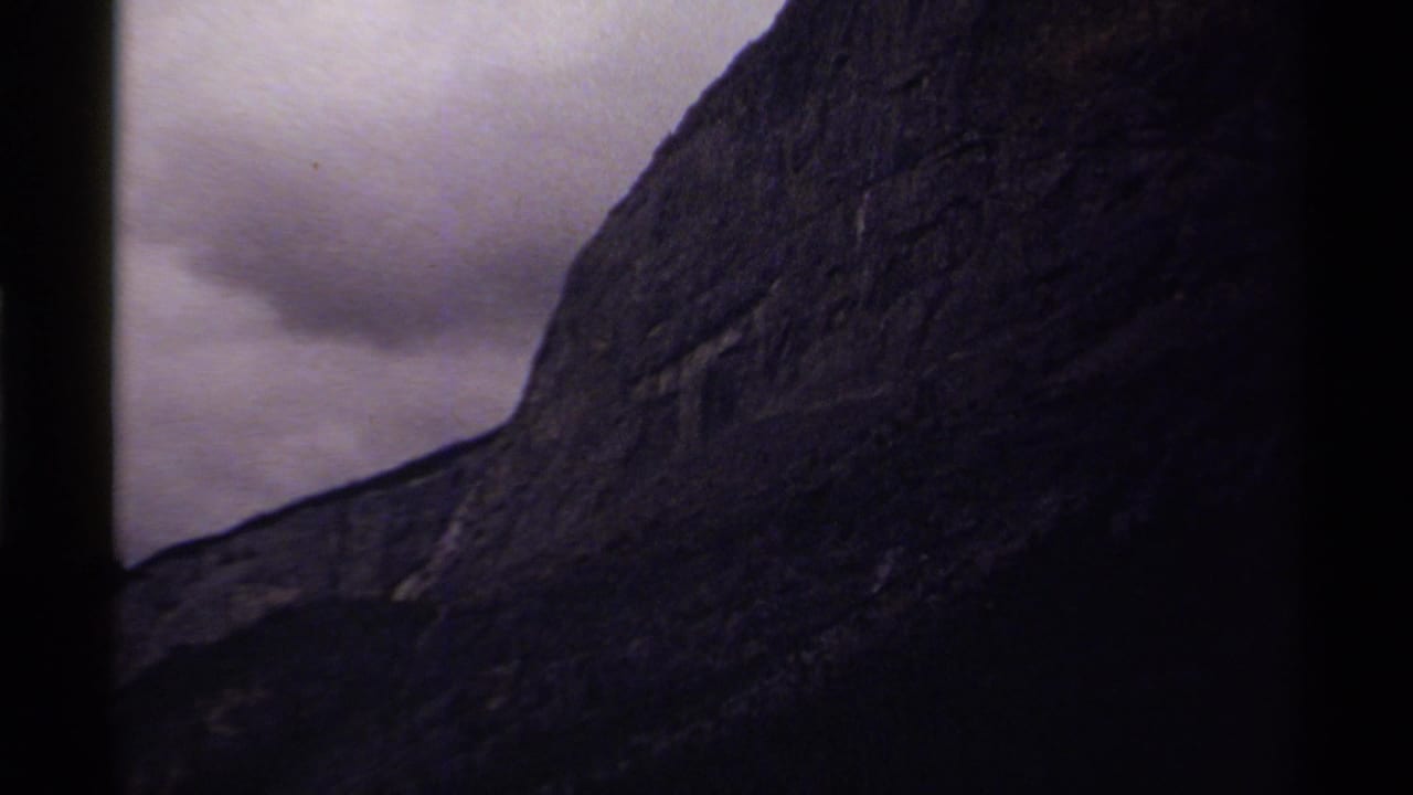 Close view of a steep mountain wall with muted clouds behind it.