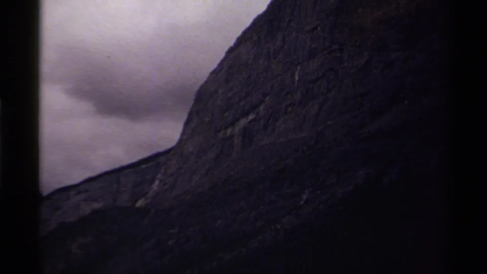 1979 Canada 8mm frame with the camera close on a textured dark mountain face against a gray, clouded sky.