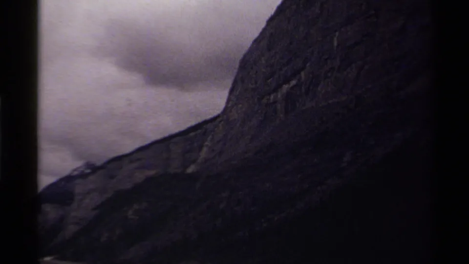 1979 Canada 8mm frame showing the mountain slope widening into darker valley forms beneath an overcast sky.