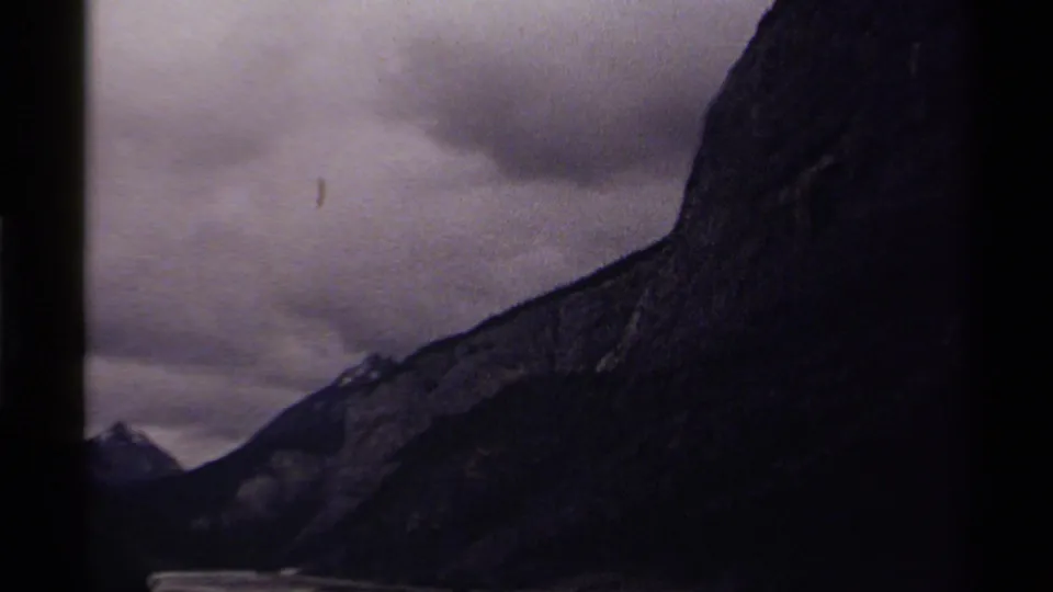 1979 Canada 8mm frame revealing a distant peak beside the dark mountain slope under heavy clouds.