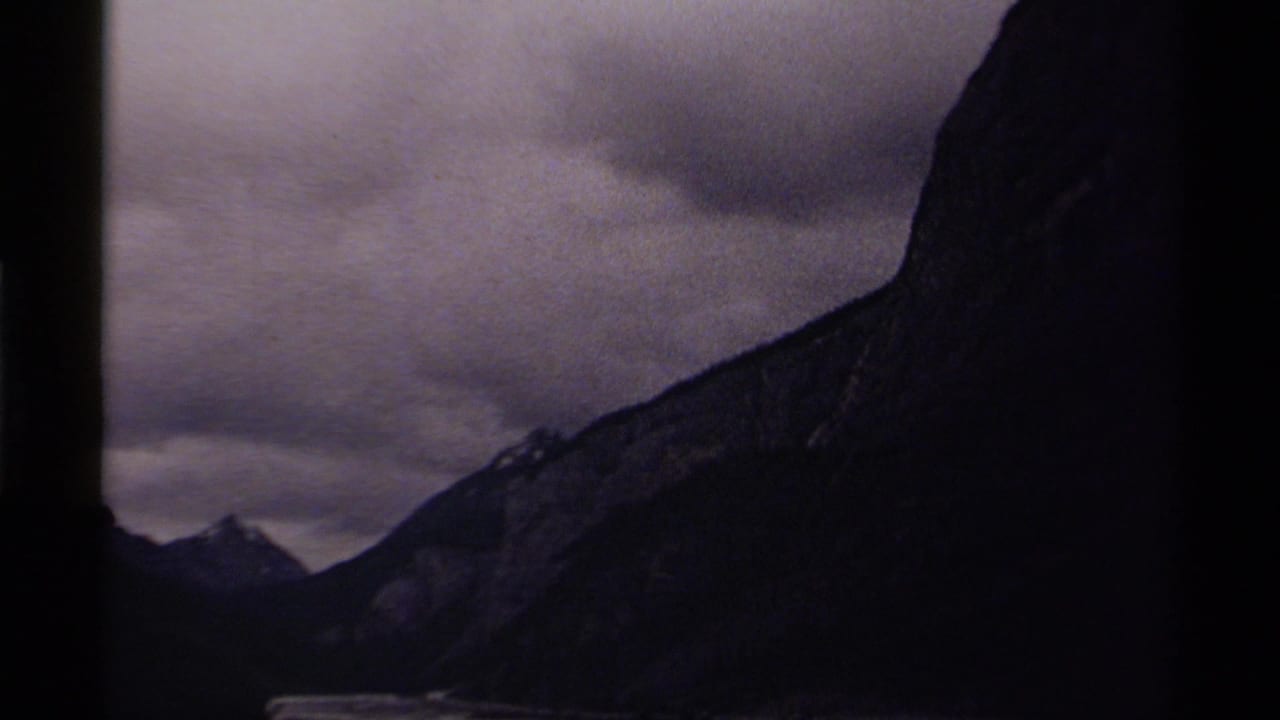 Dark mountain range beneath heavy clouds with a narrow pale water area at the base.