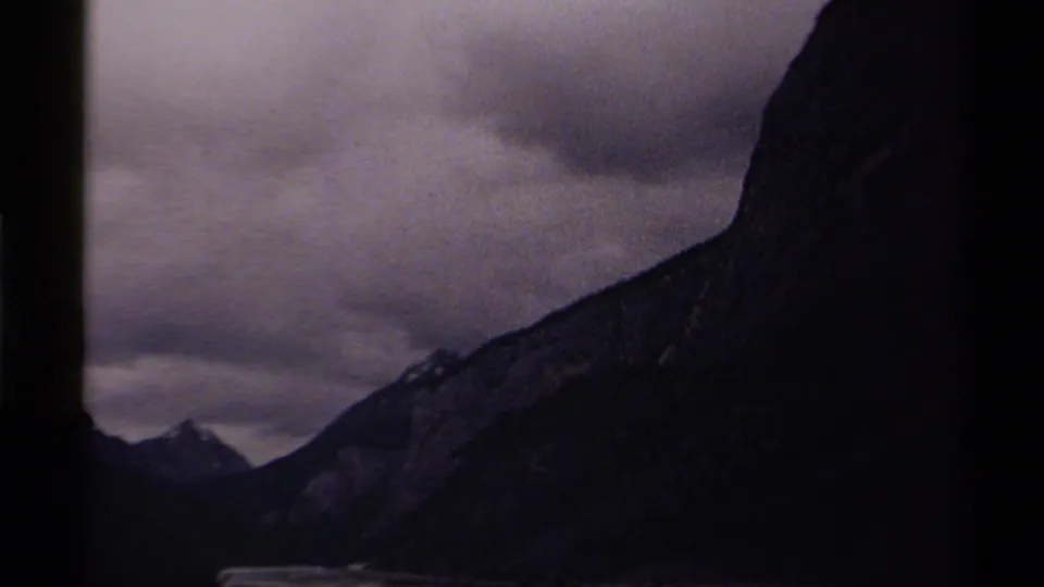 1979 8mm Canada travel footage showing silhouetted mountain peaks under dense cloud cover in low light.