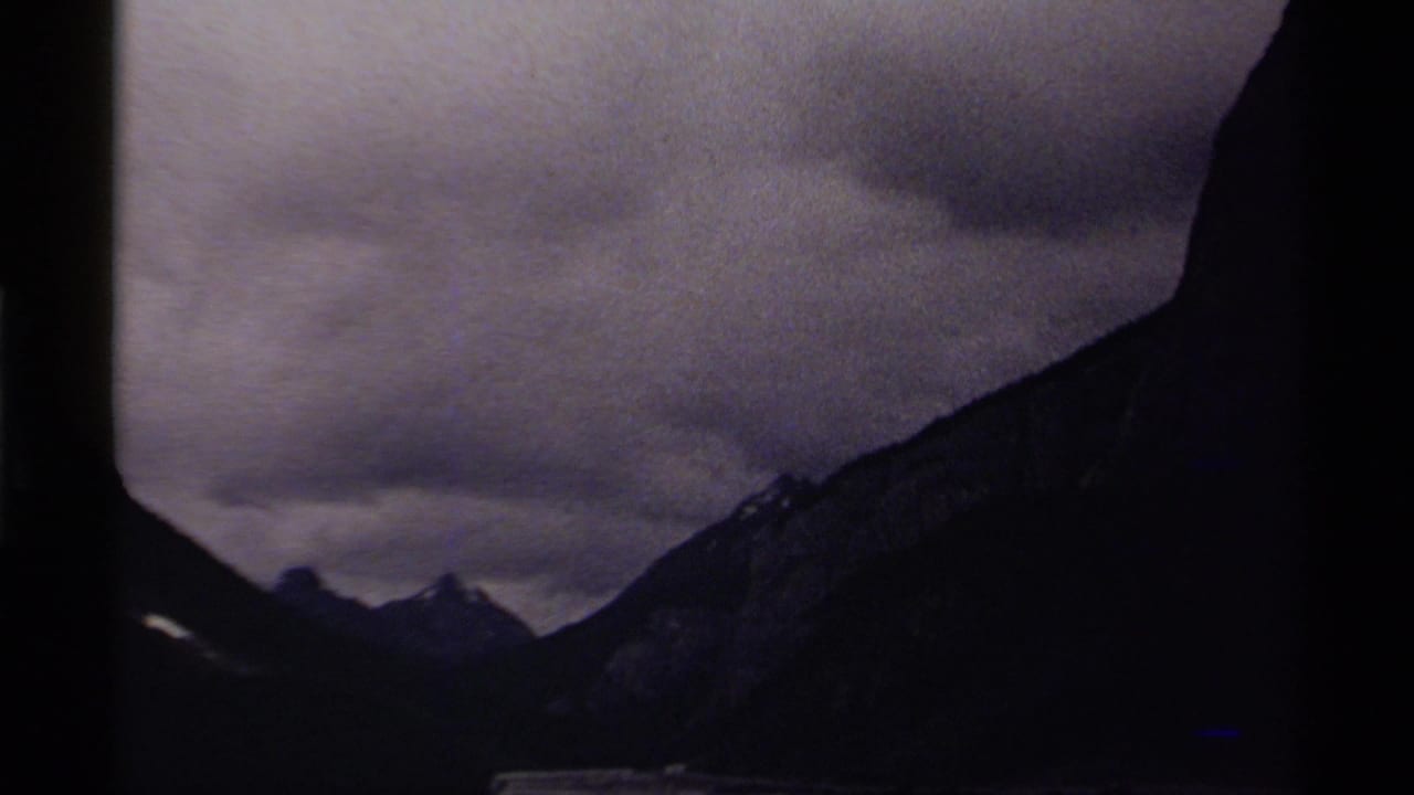 Mountain silhouettes and cloudy sky seen across a dark valley in low light.