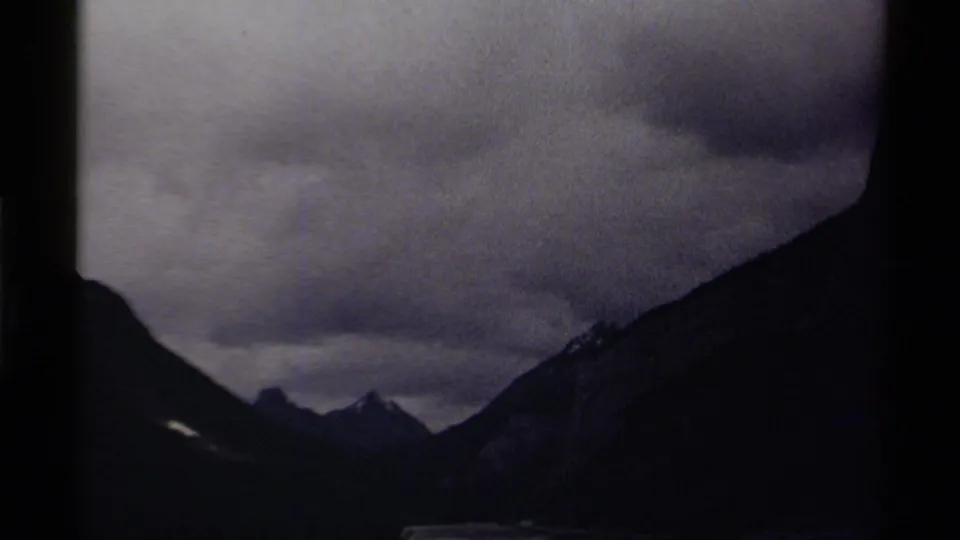Handheld 1979 Canada 8mm frame of a clouded mountain valley, dark ridges, and distant peaks.